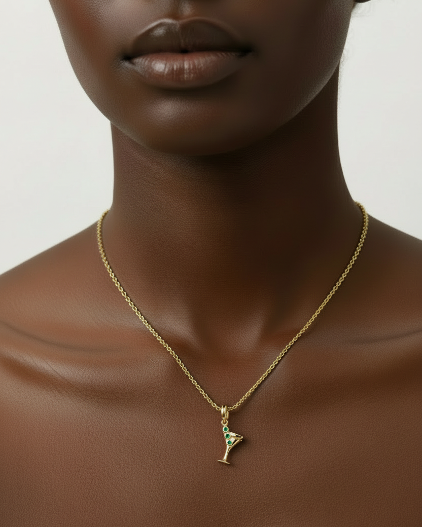 Gold martini glass pendant with emerald stones on a white background